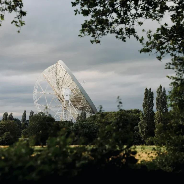 Jodrell Bank A large radio telescope, Jodrell Bank, stands against a cloudy sky, surrounded by trees.
